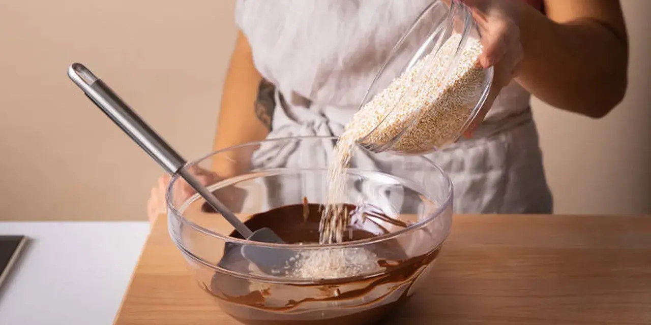Eine Person gibt Amaranth zu geschmolzener Schokolade in einer Schüssel. Was ist Amaranth? Ein gesundes Getreide für leckere Rezepte.