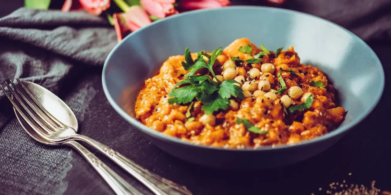 Herzhaftes Gericht mit Kichererbsen und Petersilie, verfeinert mit Garam Masala. Daneben liegen Gabel und Löffel.
