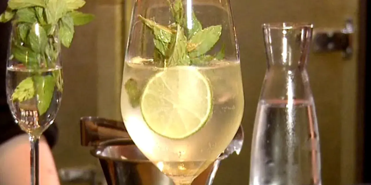 Erfrischender Hugo mit Limette und Minze, perfekt für ein Hugo Rezept. Daneben ein Glas mit Minze und eine Karaffe Wasser.