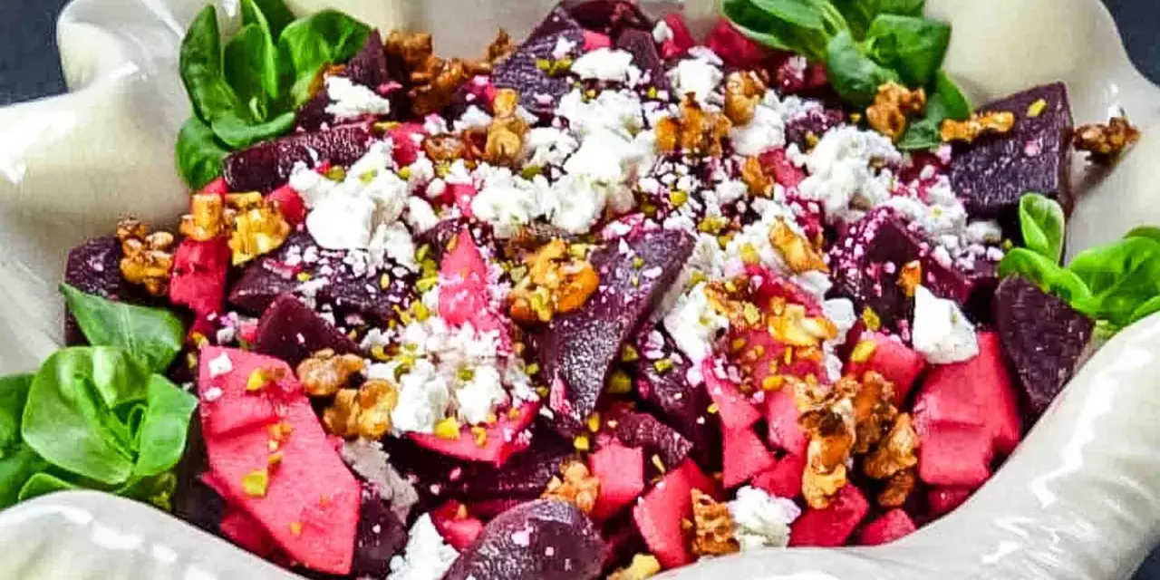 Rote Bete Salat mit Apfel, Feta und Walnüssen, garniert mit grünen Blättern. Ein farbenfroher und gesunder Genuss.