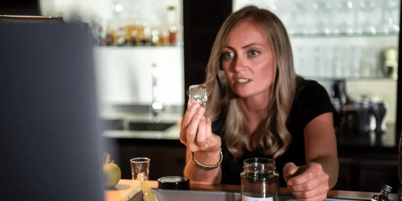 Eine Barkeeperin zeigt einen Eiswürfel, der für perfekte cocktail rezepte unerlässlich ist.