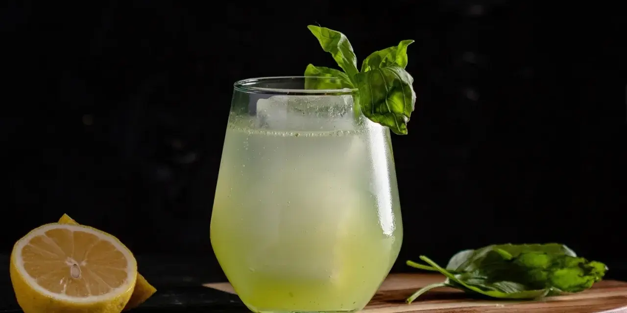 Erfrischender Basil Smash mit Zitrone und Basilikum garniert, serviert auf einem Holzbrett.