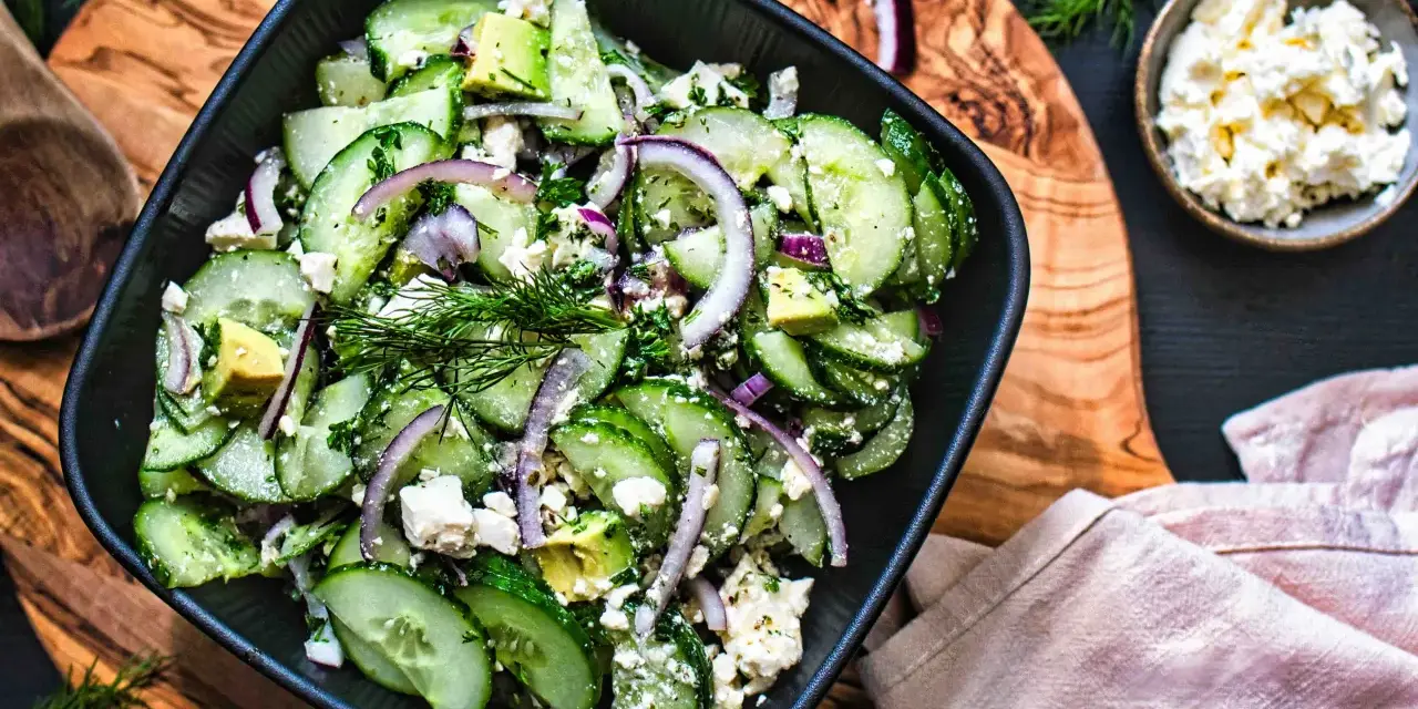 Erfrischender gurken feta salat mit Avocado, roten Zwiebeln und Dill, serviert in einer schwarzen Schüssel auf einem Holzbrett.
