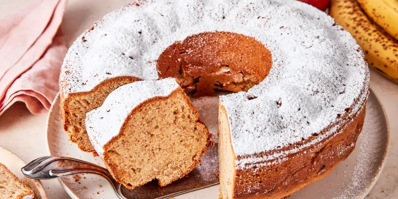 Saftiger Apfel-Bananen-Kuchen, bestäubt mit Puderzucker. Daneben liegen frische Äpfel und Bananen.