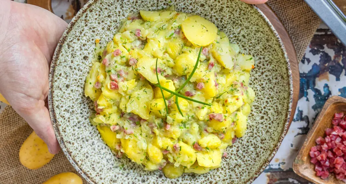 Ein Teller mit herzhaftem Kartoffelsalat mit Speck und frischen Kräutern, bereit zum Servieren.