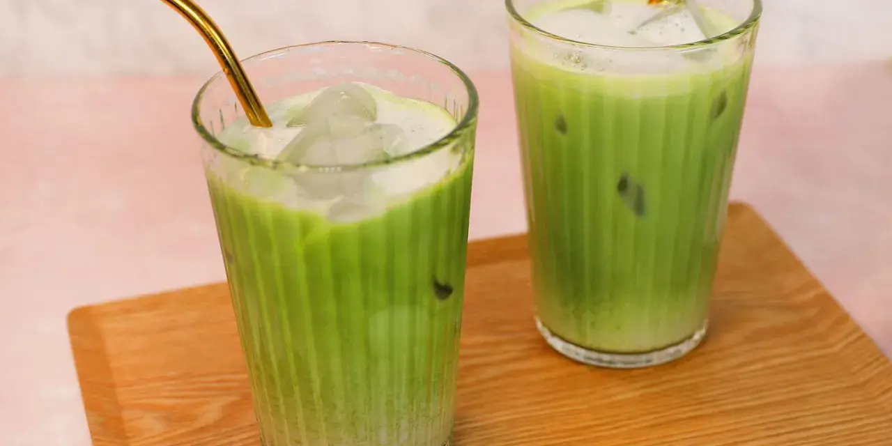 Zwei erfrischende Iced Matcha Latte mit goldenen Strohhalmen auf einem Holztablett. Perfekt für ein schnelles iced matcha latte rezept.