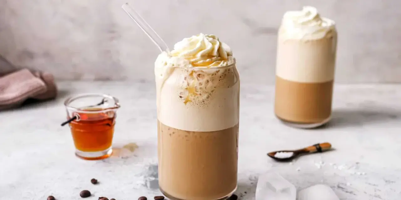 Eiskaffee selbst machen: Ein erfrischender Eiskaffee mit Sahne und Sirup, daneben Kaffeebohnen und Eiswürfel.