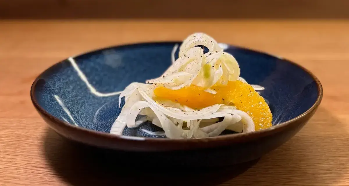 Ein erfrischender Fenchel-Orangen-Salat, garniert mit Pfeffer, in einer blauen Schale auf einem Holztisch.
