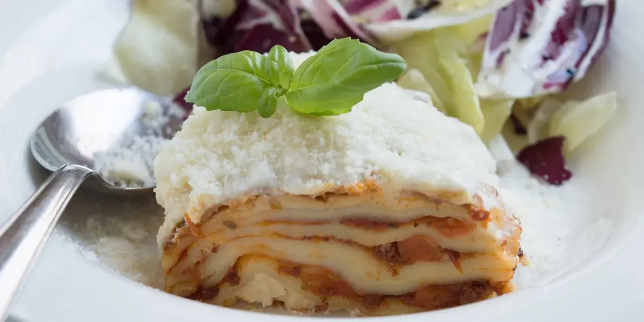 Ein Stück Lasagne mit Schmand, garniert mit Basilikum und Parmesan, serviert mit einem Salat.