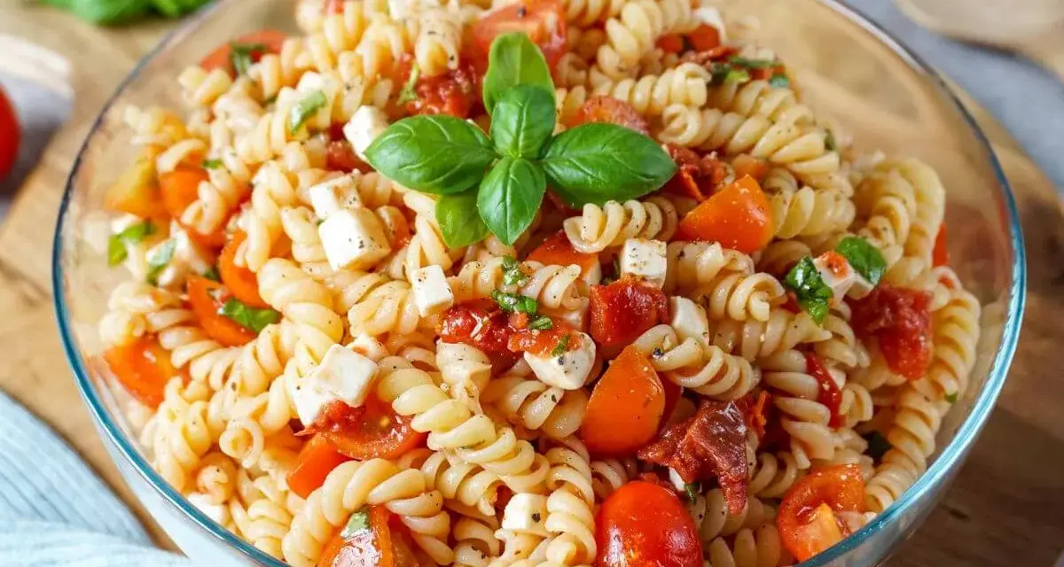 Ein köstlicher mediterraner Nudelsalat mit Fusilli, Kirschtomaten, Mozzarella und Basilikum, garniert mit frischen Basilikumblättern.