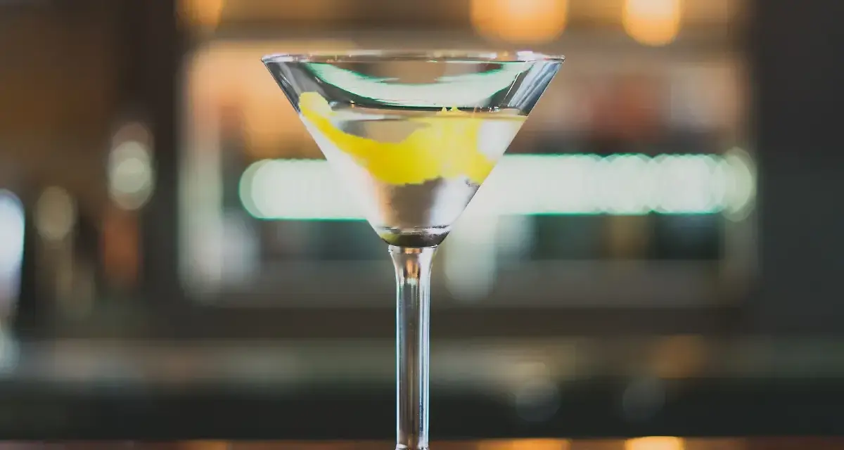 Ein klassischer Martini, perfekt für Ihr Martini Rezept. Mit Zitronenzeste garniert, steht er auf einer Holztheke.