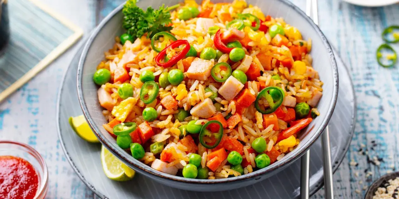 Schüssel mit Nasi Goreng: gebratener Reis mit Hühnchen, Erbsen, Karotten, Chili und Limettenspalten.