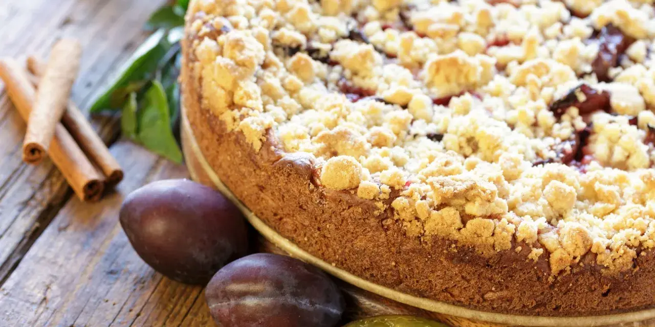 Ein saftiger Zwetschgenkuchen mit knusprigen Streuseln, daneben frische Zwetschgen und Zimtstangen. Perfekt für ein Streusel Rezept einfach!