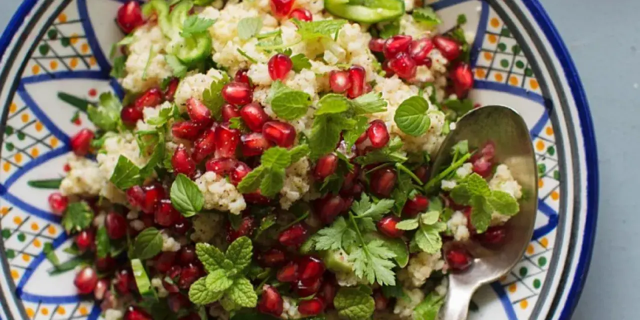 Bunter Couscous-Salat mit Granatapfelkernen, Minze und Petersilie in einer orientalisch gemusterten Schale.