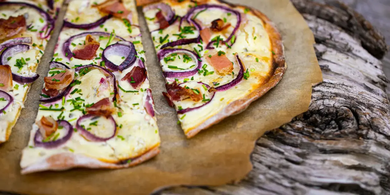 Flammkuchen mit klassischem Belag: Speck, Zwiebeln und Schnittlauch auf knusprigem Teig.