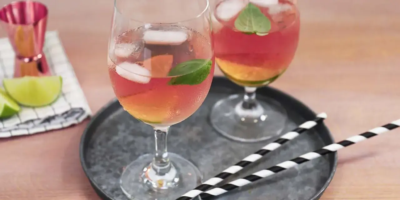 Zwei Gläser Rosato Spritz mit Eis und Minze, dazu Limettenspalten und ein Messbecher. Perfekt für einen sommerlichen Genuss.