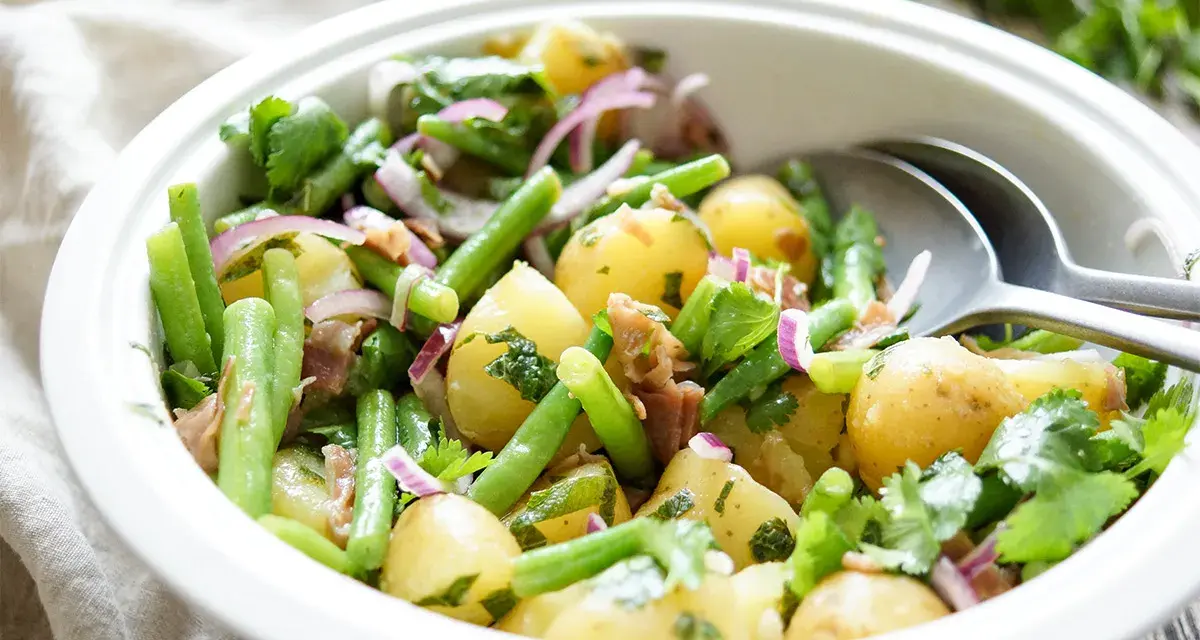 Frischer Kartoffel Bohnen Salat mit roten Zwiebeln und Kräutern in einer weißen Schüssel, bereit zum Servieren.