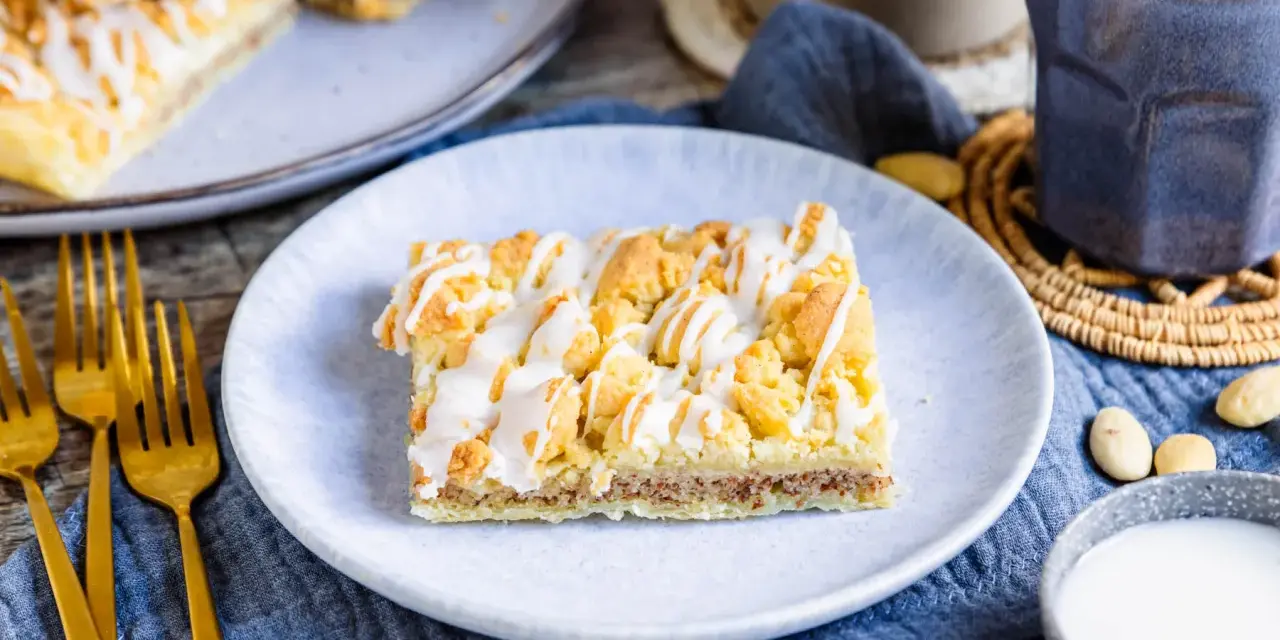 Ein Stück Prasselkuchen, wie aus einem DDR-Rezept, mit Zuckerguss und Streuseln. Dazu Kaffee und Mandeln.