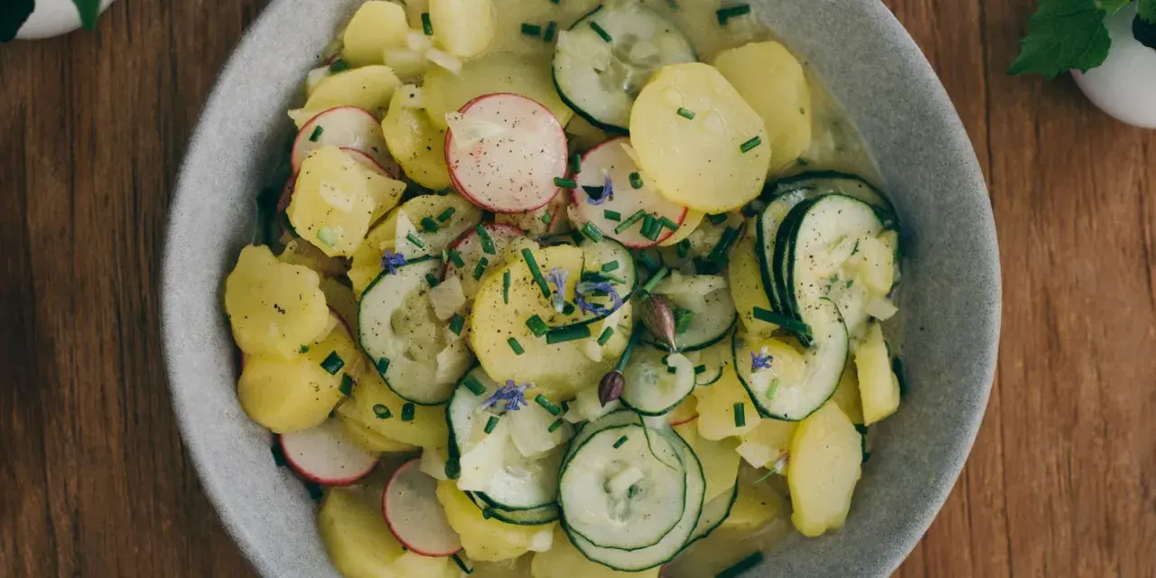 Ein Teller mit lauwarmer bayrischer Kartoffelsalat, garniert mit Radieschen, Gurken und Schnittlauch.