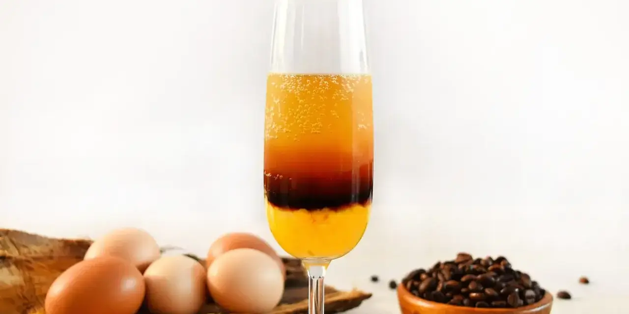 Schicht-Cocktail mit Ei, Kaffee und Orangensaft. Daneben liegen Eier und Kaffeebohnen.