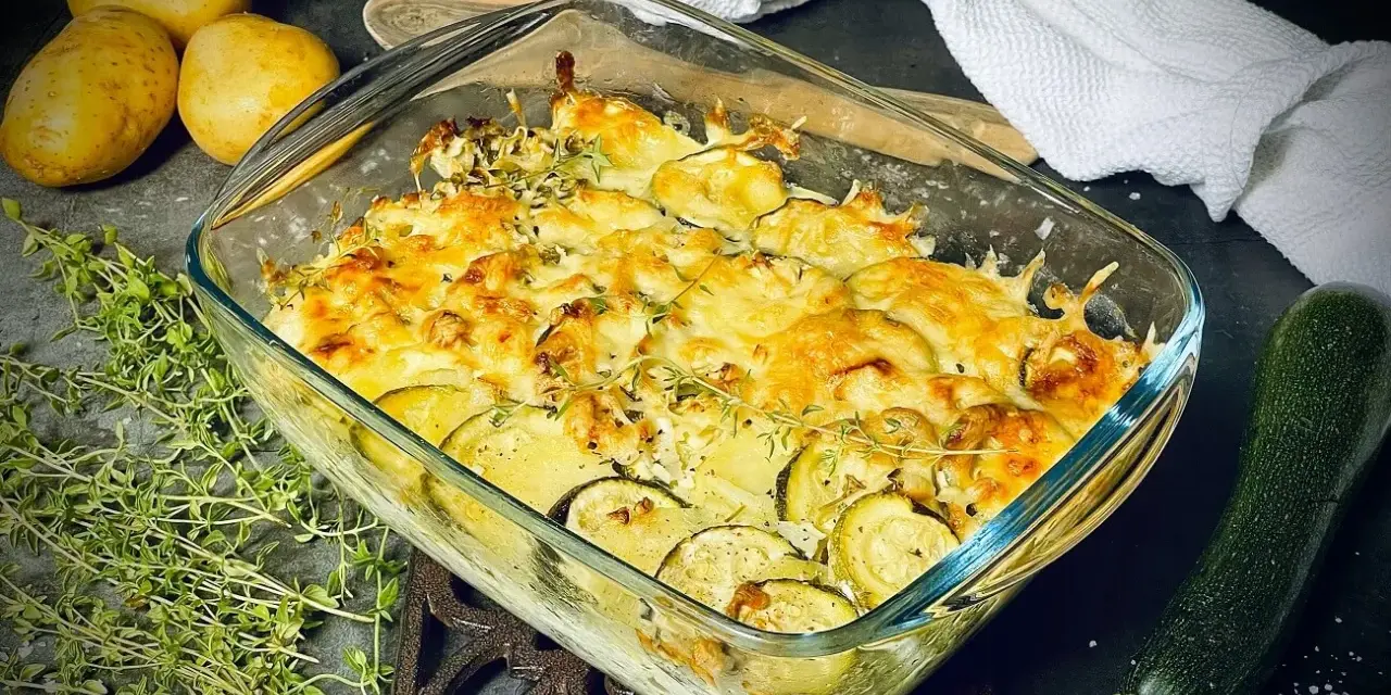 Goldbrauner Zucchini-Kartoffel-Auflauf mit Käse überbacken, garniert mit frischem Thymian. Daneben liegen Kartoffeln und eine Zucchini.