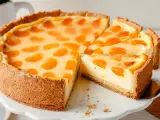 Ein saftiger Schmandkuchen mit Mandarinen, der auf einem weißen Tortenständer präsentiert wird. Ein Stück wurde bereits entnommen.