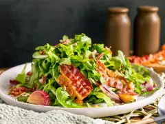 Warmer Rucolasalat mit knusprigem Speck, gerösteten Zwiebeln und Sonnenblumenkernen. Ein köstliches Gericht für Rucola Rezepte warm.