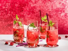Vier erfrischende Bacardi Razz Mojitos mit Himbeeren und Minze, bereit zum Genießen.