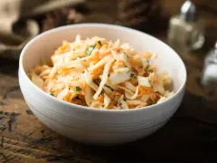Schüssel mit cremigem Rettichsalat mit Apfel und Kräutern, serviert auf einem rustikalen Holztisch.