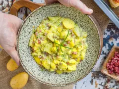 Ein Teller mit herzhaftem Kartoffelsalat mit Speck und frischen Kräutern, bereit zum Servieren.