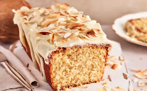 Saftiger Kuchen mit Kokosmilch, überzogen mit weißer Glasur und garniert mit gerösteten Kokoschips. Daneben eine Kokosnuss.
