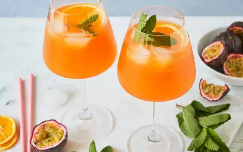 Zwei erfrischende Maracuja Spritz Cocktails mit Eis, Orangenscheiben und Minze, garniert mit frischen Passionsfrüchten.