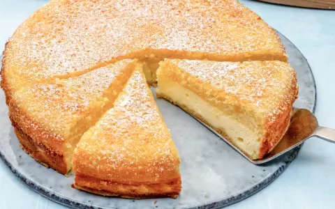 Ein saftiger Käsekuchen, bestäubt mit Puderzucker. Ein Stück wird gerade mit einem Tortenheber herausgehoben. Dreh dich um, Kuchen, du siehst köstlich aus!