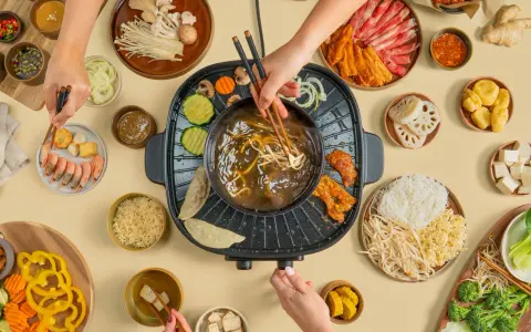Hände greifen nach Zutaten für einen Hot Pot. Fleisch, Gemüse, Garnelen und Nudeln werden in die köchelnde Brühe getaucht.