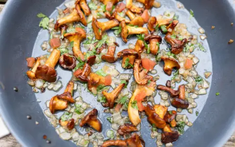 Pfifferlinge rezept: Goldgelbe Pfifferlinge braten mit Zwiebeln und Petersilie in einer Pfanne. Ein köstliches Gericht!