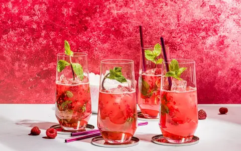 Vier erfrischende Bacardi Razz Mojitos mit Himbeeren und Minze, bereit zum Genießen.