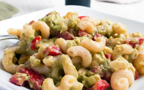 Cremiger nudelsalat mit avocado, Tomaten und Gewürzen auf einem weißen Teller.