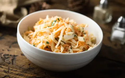 Schüssel mit cremigem Rettichsalat mit Apfel und Kräutern, serviert auf einem rustikalen Holztisch.
