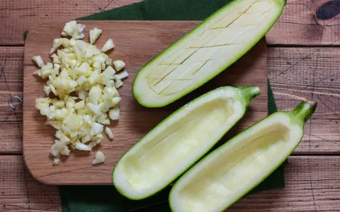 Vorbereitung für gefüllte Zucchini: ausgehöhlte Zucchinihälften und gehackter Knoblauch liegen bereit. Die Zucchini kerne essbar, werden oft mitverwendet.