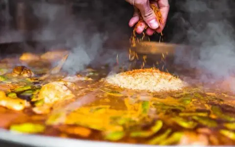 Gewürze werden über Reis und Gemüse gestreut, was zeigt, was ist paella: ein köstliches spanisches Reisgericht, das in einer großen Pfanne gekocht wird.
