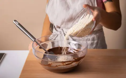 Eine Person gibt Amaranth zu geschmolzener Schokolade in einer Schüssel. Was ist Amaranth? Ein gesundes Getreide für leckere Rezepte.