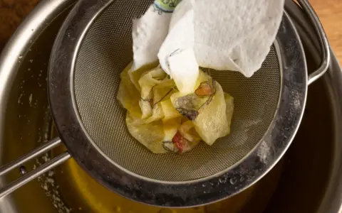 Ein Sieb hält ein Stück Papier mit Blumenmuster, das über einem Topf mit geschmolzener Butter liegt. Perfekt für raffinierte Butter Rezepte.