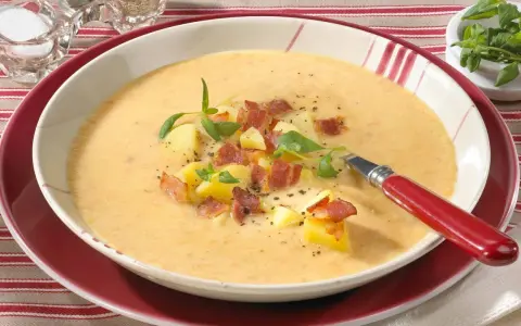 Eine dampfende, cremige Kartoffelsuppe mit Sahne, garniert mit Kartoffelwürfeln, knusprigem Speck und frischen Kräutern.