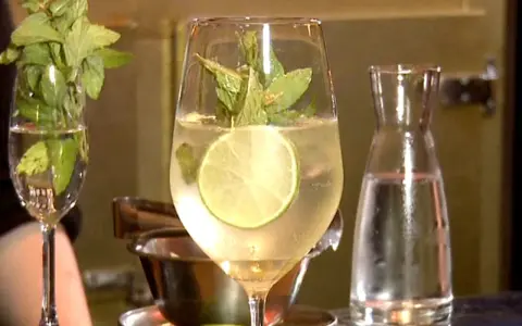 Erfrischender Hugo mit Limette und Minze, perfekt für ein Hugo Rezept. Daneben ein Glas mit Minze und eine Karaffe Wasser.
