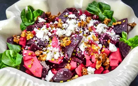 Rote Bete Salat mit Apfel, Feta und Walnüssen, garniert mit grünen Blättern. Ein farbenfroher und gesunder Genuss.