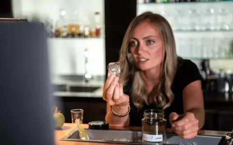 Eine Barkeeperin zeigt einen Eiswürfel, der für perfekte cocktail rezepte unerlässlich ist.