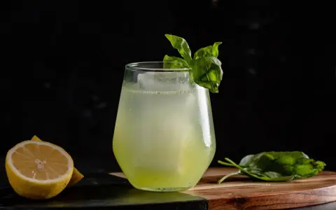 Erfrischender Basil Smash mit Zitrone und Basilikum garniert, serviert auf einem Holzbrett.