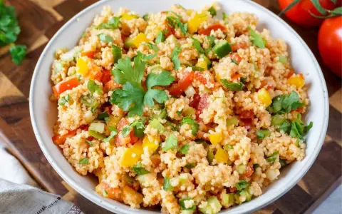 Frischer Couscous Salat mit Tomaten, Paprika und Petersilie, garniert mit einem Petersilienblatt.