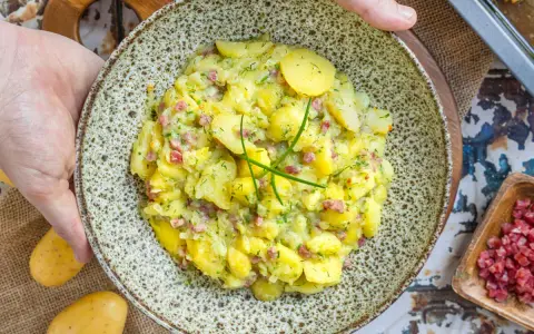 Ein Teller mit herzhaftem Kartoffelsalat mit Speck und frischen Kräutern, bereit zum Servieren.