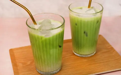 Zwei erfrischende Iced Matcha Latte mit goldenen Strohhalmen auf einem Holztablett. Perfekt für ein schnelles iced matcha latte rezept.